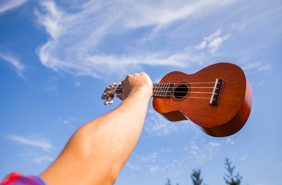 a raised hand holding a ukulele with a blue sky in the background