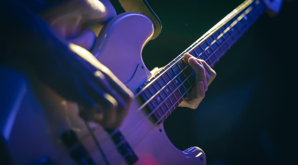 A guitarist's hand playing a white electric guitar under blue stage lighting