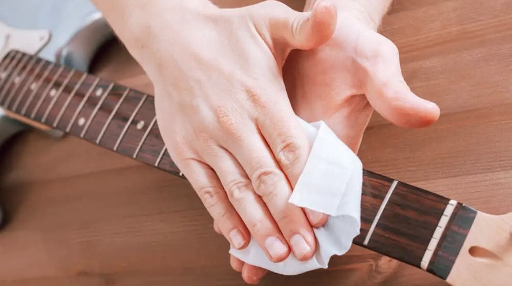 Hand cleaning guitar fretboard with napkin