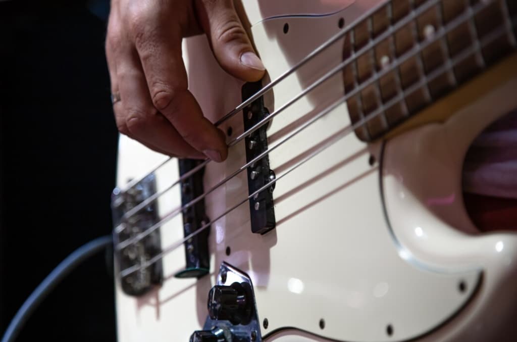 Close-up of a musician's hand adjusting the strings on a white bass guitar