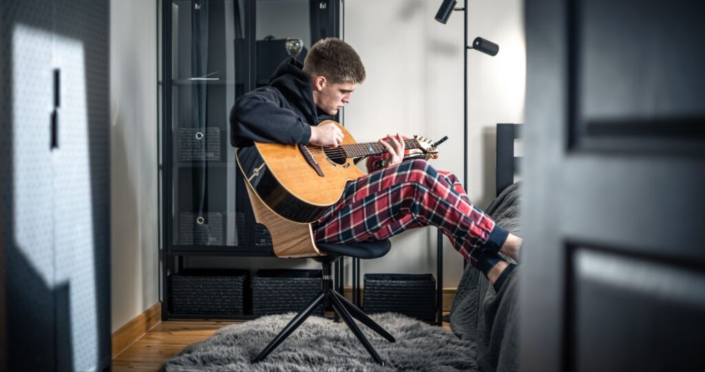 Young man plays the acoustic guitar in his room at home