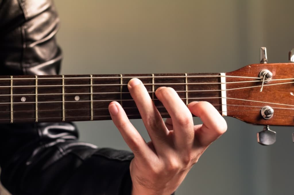 Close-up of a hand forming a chord on the fretboard of a ukulele