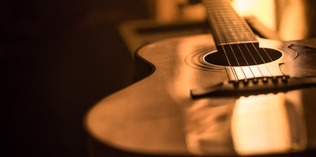A guitar resting in a dimly lit room, highlighting its sound hole and strings
