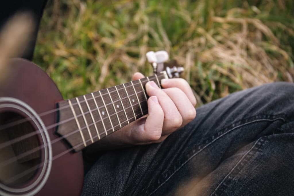 Close view of a person's hand strumming a ukulele resting on their lap outdoors