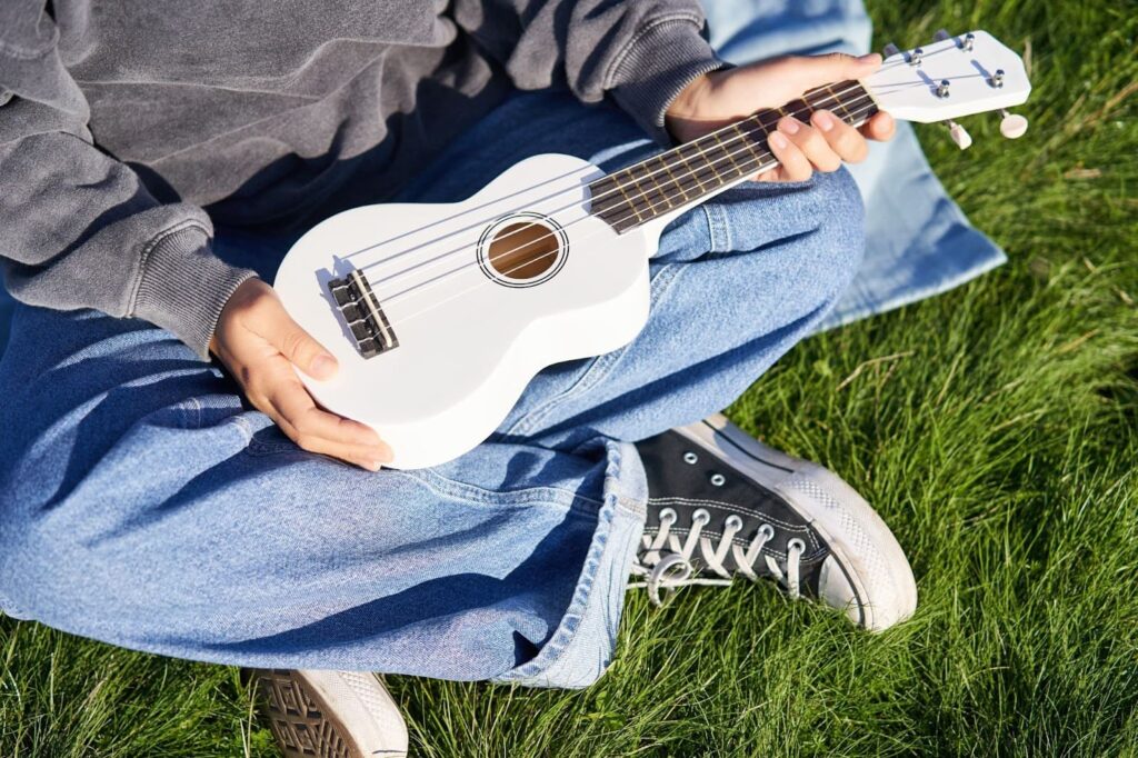 a person holding a white ukulele while sitting on the grass