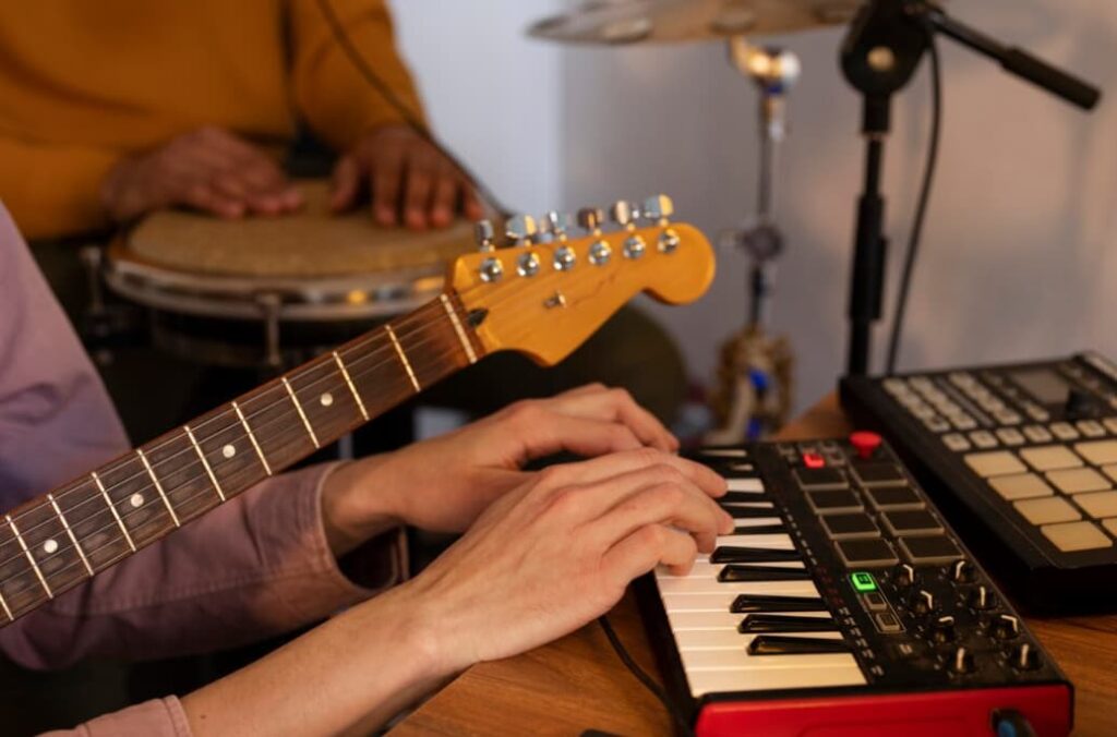 Musician's hands playing a keyboard with a guitar and drums in the background
