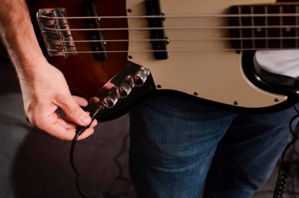 A person's hand plugging a cable into an electric bass guitar