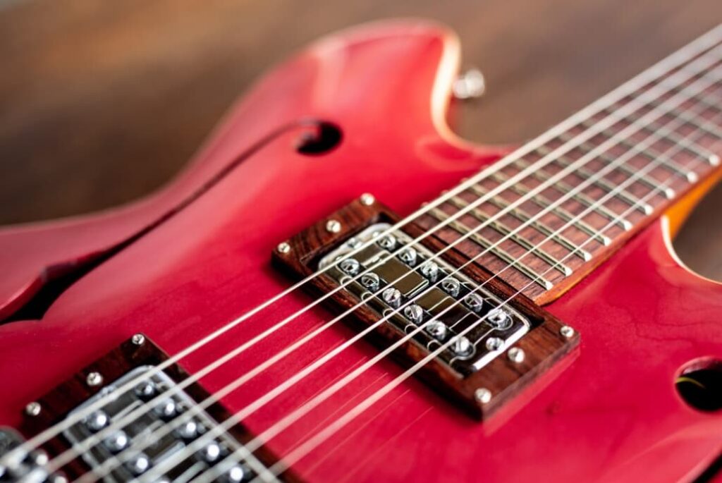 A close-up of a red electric bass guitar, showcasing its bridge, pickups, and strings
