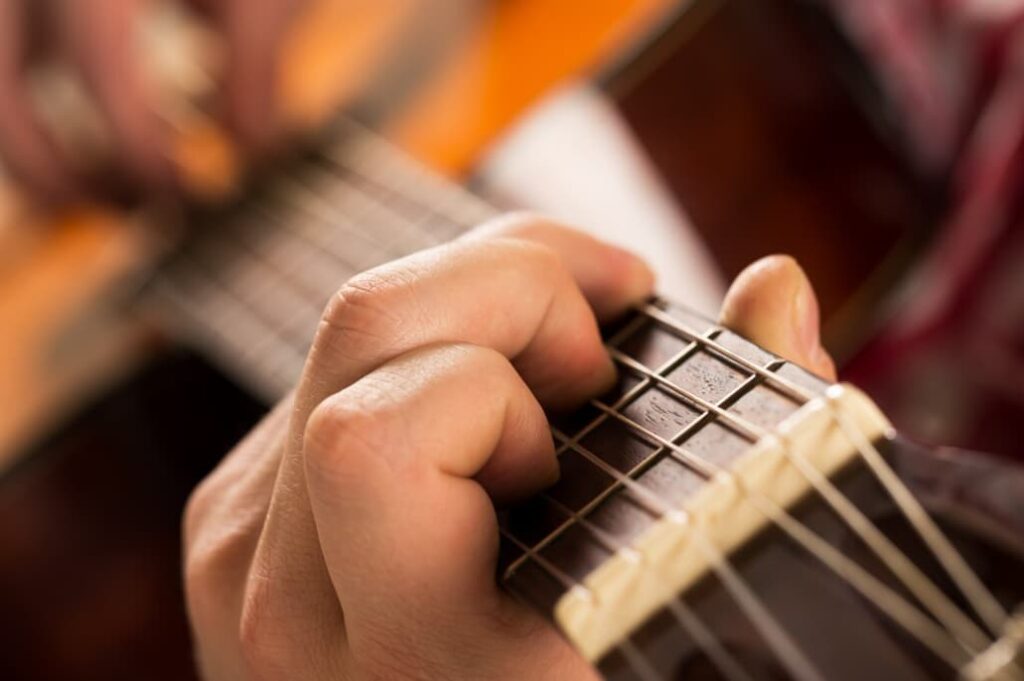 A person's hand forming chords on the fretboard of a guitar, with a focus on the fingers