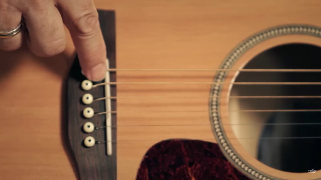 An acoustic guitar bridge and strings with a hand