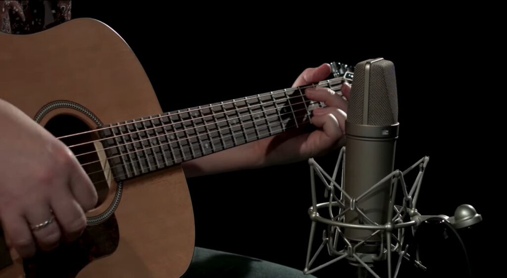 A person playing an acoustic guitar with a microphone in front