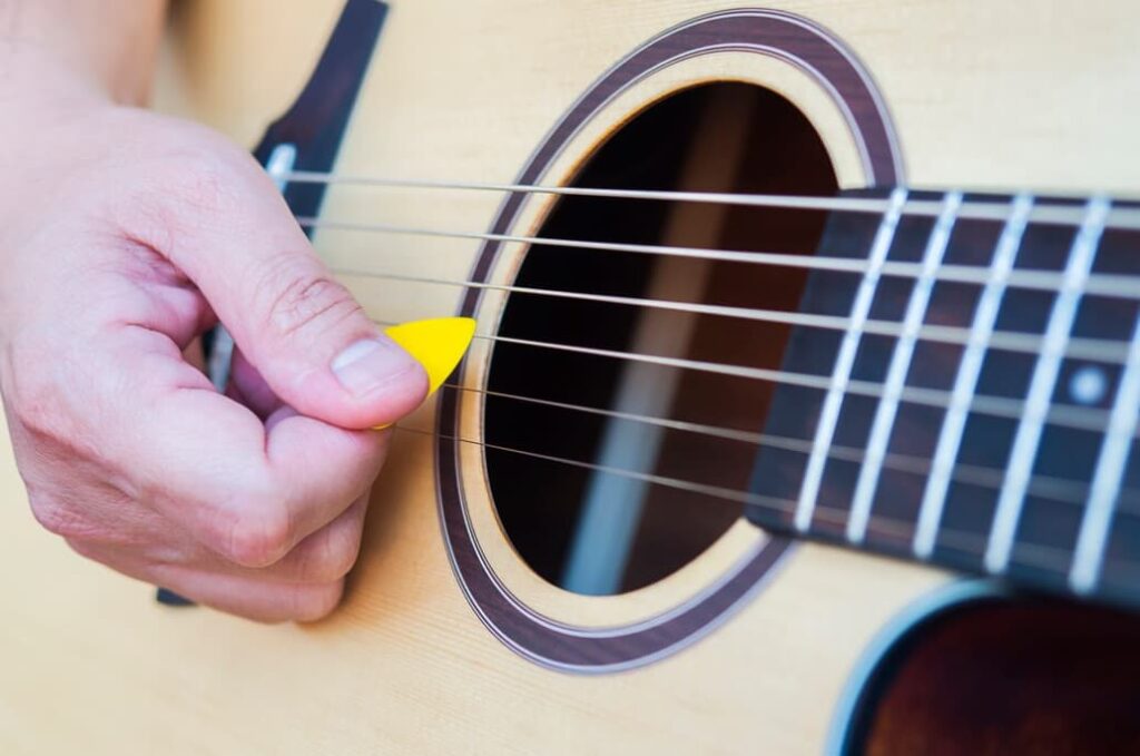 A hand strumming the strings of an acoustic guitar with a pick