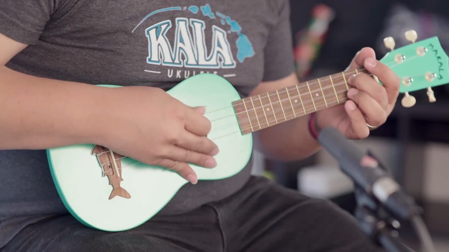 A person strumming a mint green ukulele with a dolphin-shaped soundhole